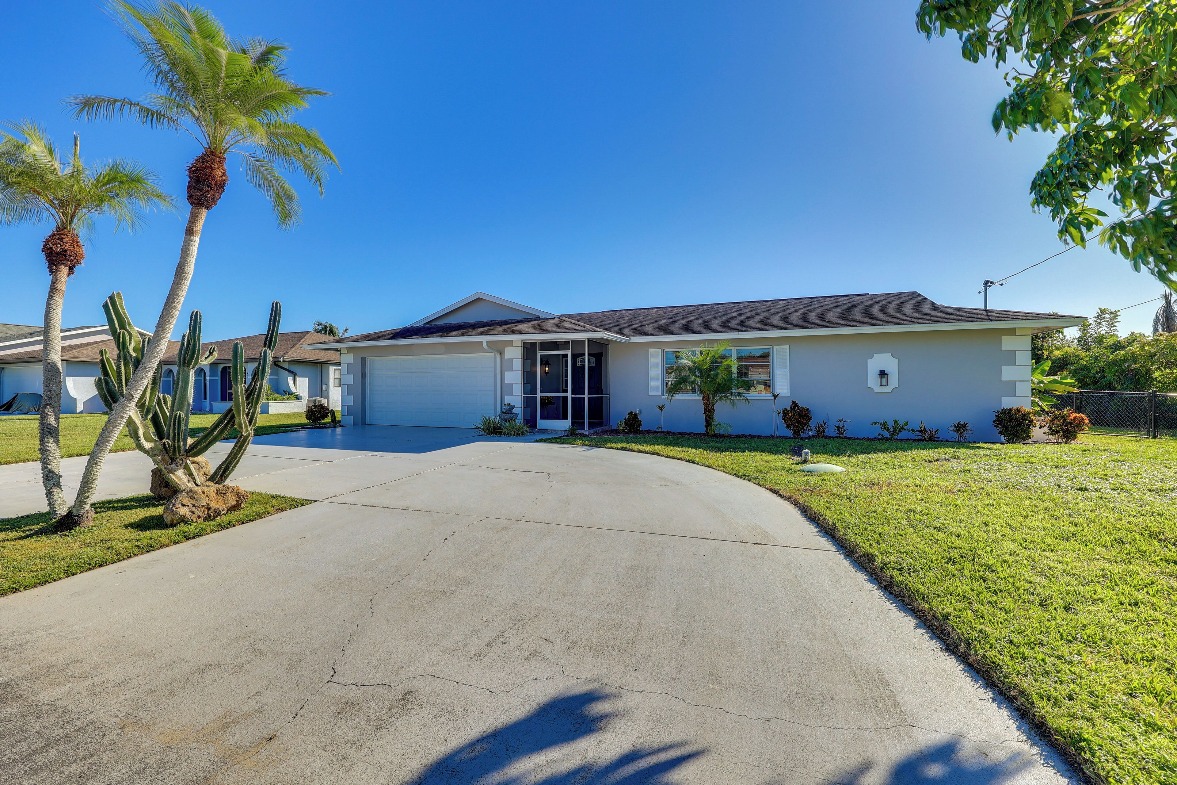 A residential house with a driveway, palm trees, and a lawn.