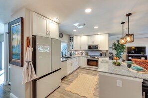 A modern kitchen with white cabinetry, a granite countertop, a built-in oven, and a dining area with a red sofa. - North Fort Myers Waterfront Home w/ Pool & Dock (North Fort Myers)