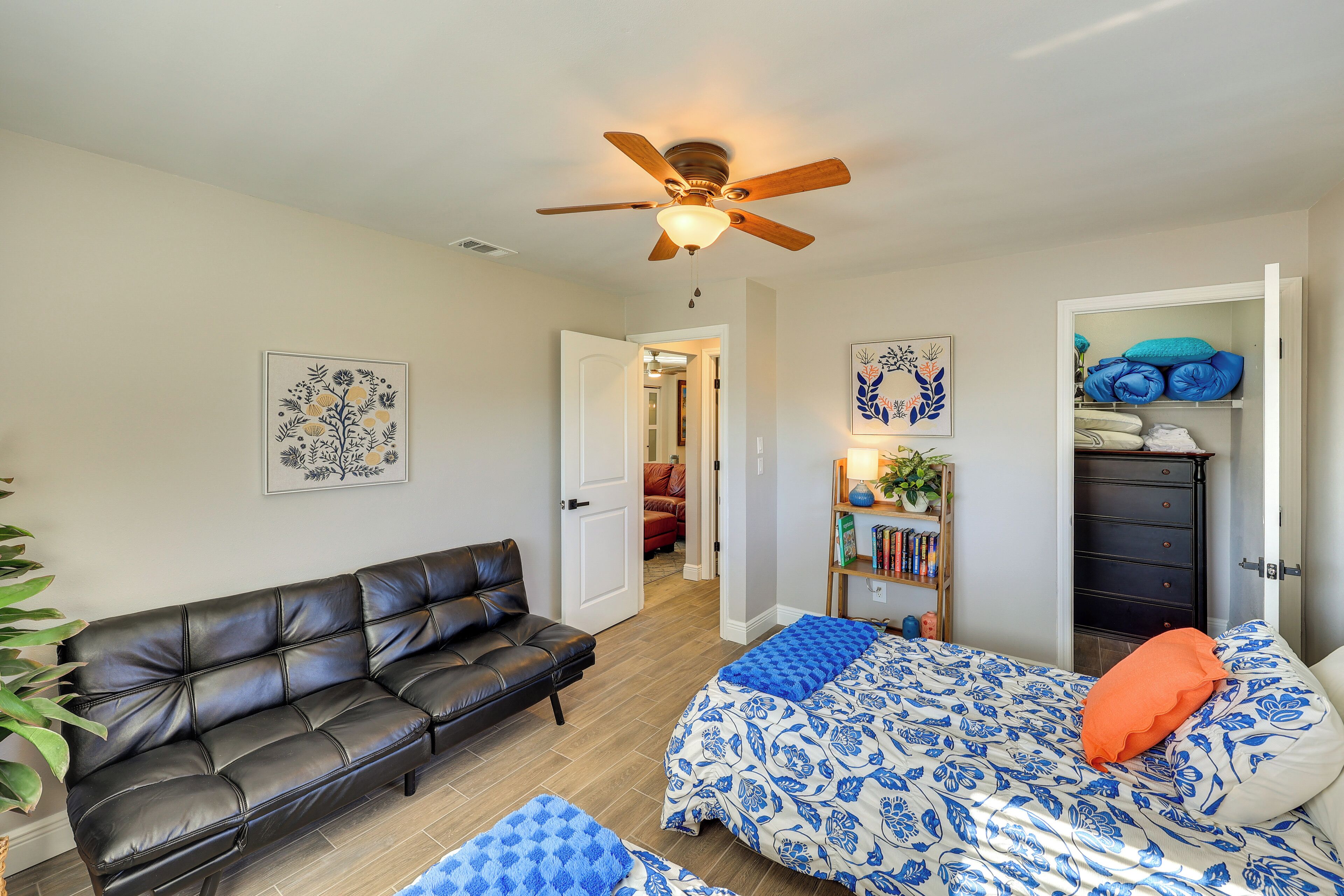 A bedroom with a bed, a sofa, a ceiling fan, and a dresser.