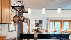 A modern kitchen with wooden cabinets, a black countertop, hanging pots, and pendant lights. - The Magic Teacup:  Steps from the Slopes and Trails! (Davis)