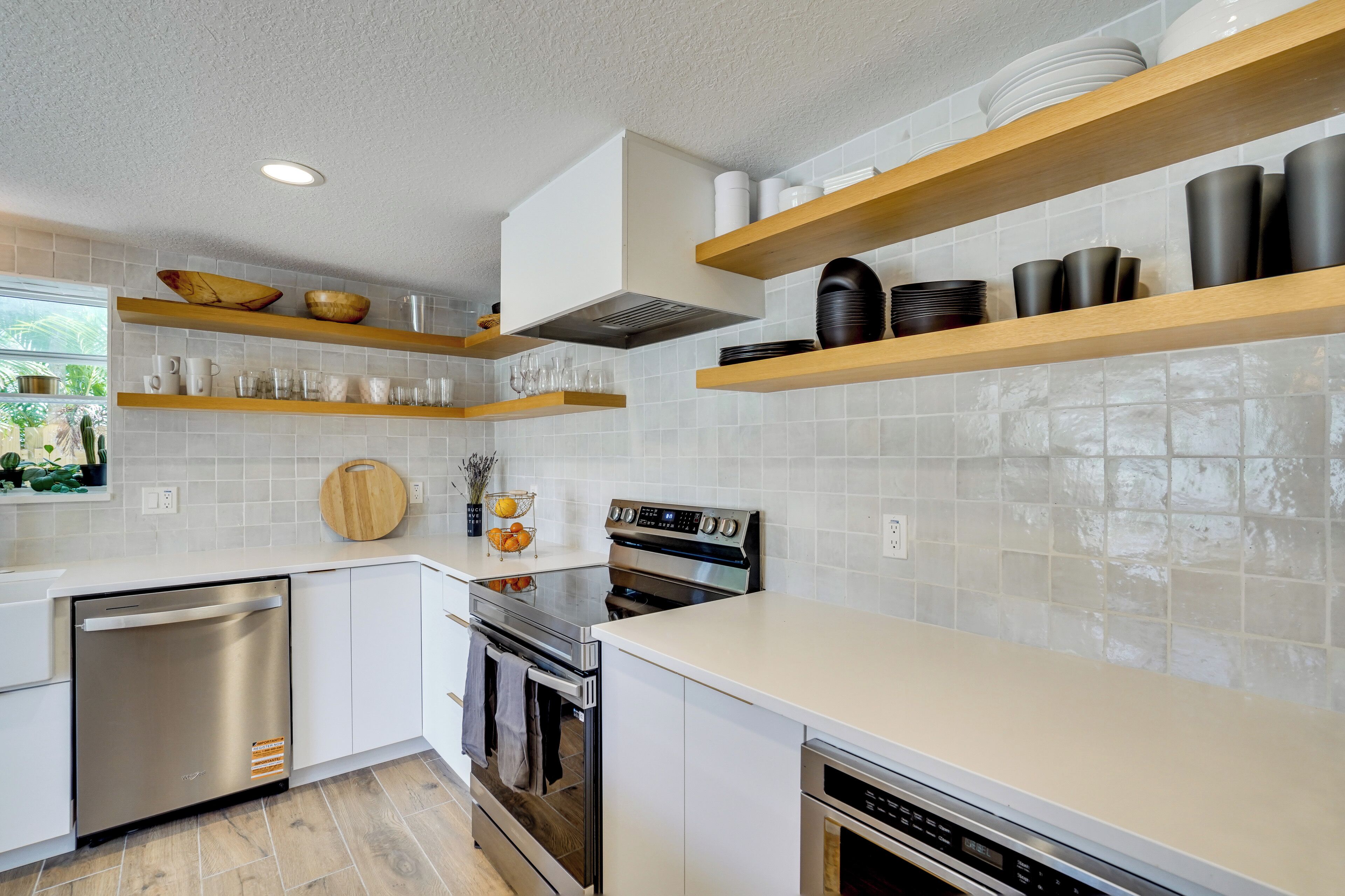 A modern kitchen with white cabinetry, stainless steel appliances, and wooden shelves.