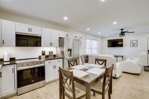 A modern kitchen with white cabinetry, a built-in oven, and a dining area with a wooden table and chairs. - Wooded Retreat w/ Pet-friendly Yard in Standish (Standish)