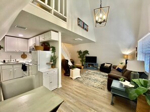 Amplia sala de estar con cocina, una escalera, un sofá y una televisión.