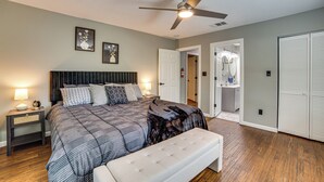 A bedroom with a bed, a bench, a ceiling fan, and a door leading to a bathroom. - Walk to East Texas A&m! Home w/ Pet-friendly Yard (Commerce)