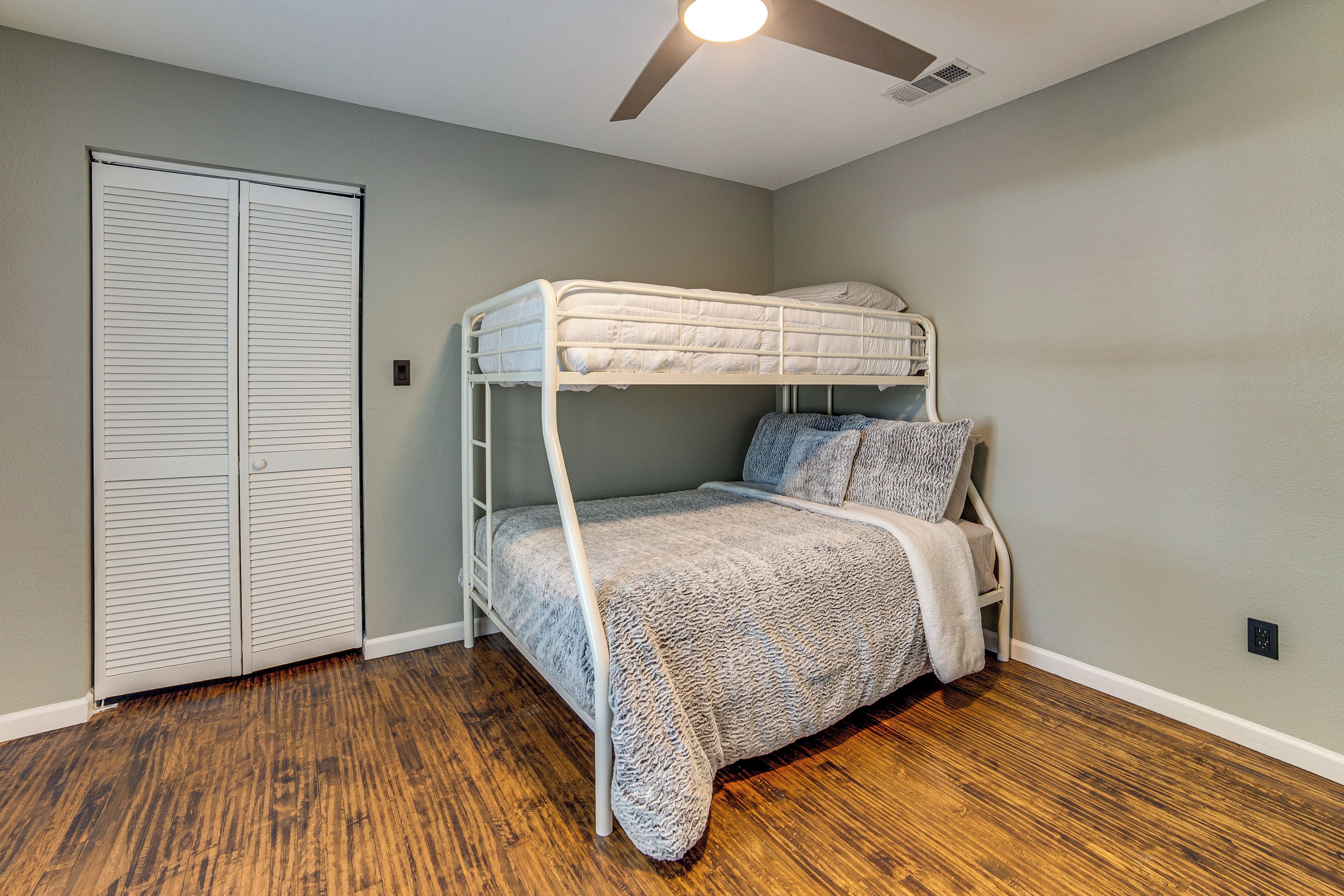 Una cama litera en una habitación con piso de madera, ventilador de techo y armario.