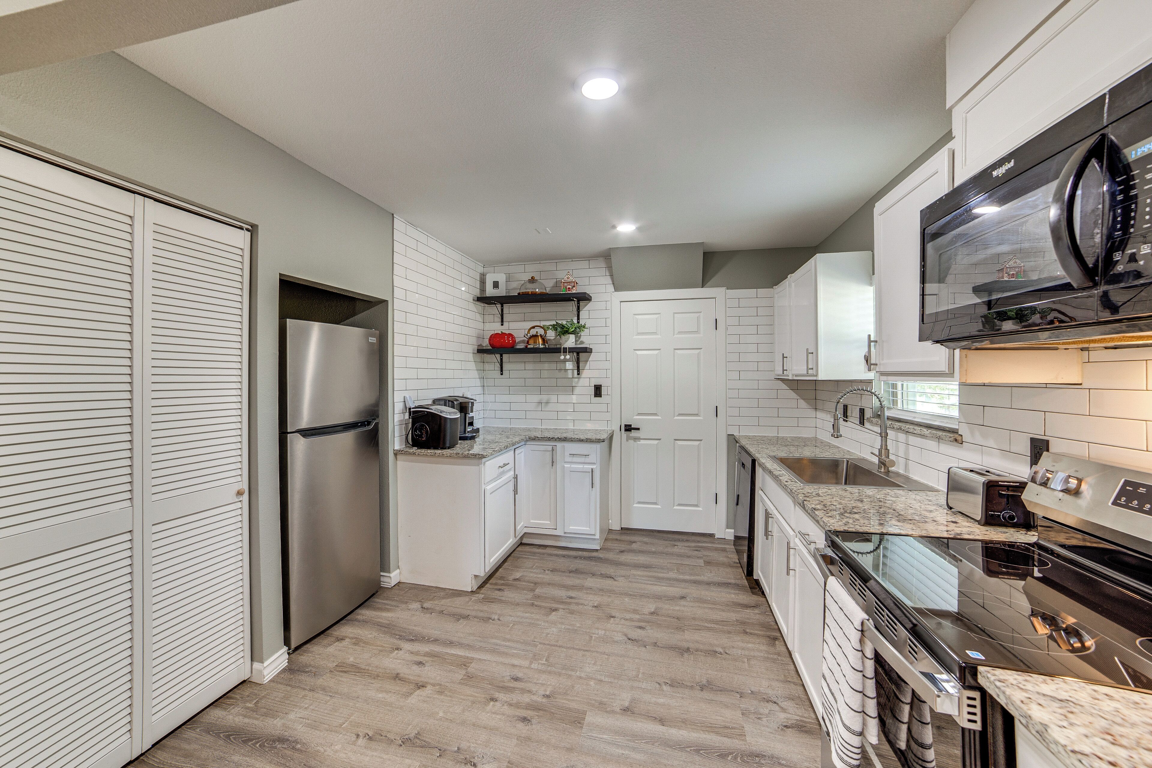 A modern kitchen with white cabinets, stainless steel appliances, and a wooden floor.