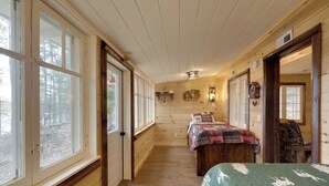 Ein gemütliches Blockhaus-Interieur mit Holzboden, einem Bett mit grüner Steudecke, einer Bank und einem Kamin.