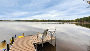 Eine Holzsteg mit Tisch und zwei Stühlen, mit Blick auf einen ruhigen See mit Bäumen im Hintergrund.