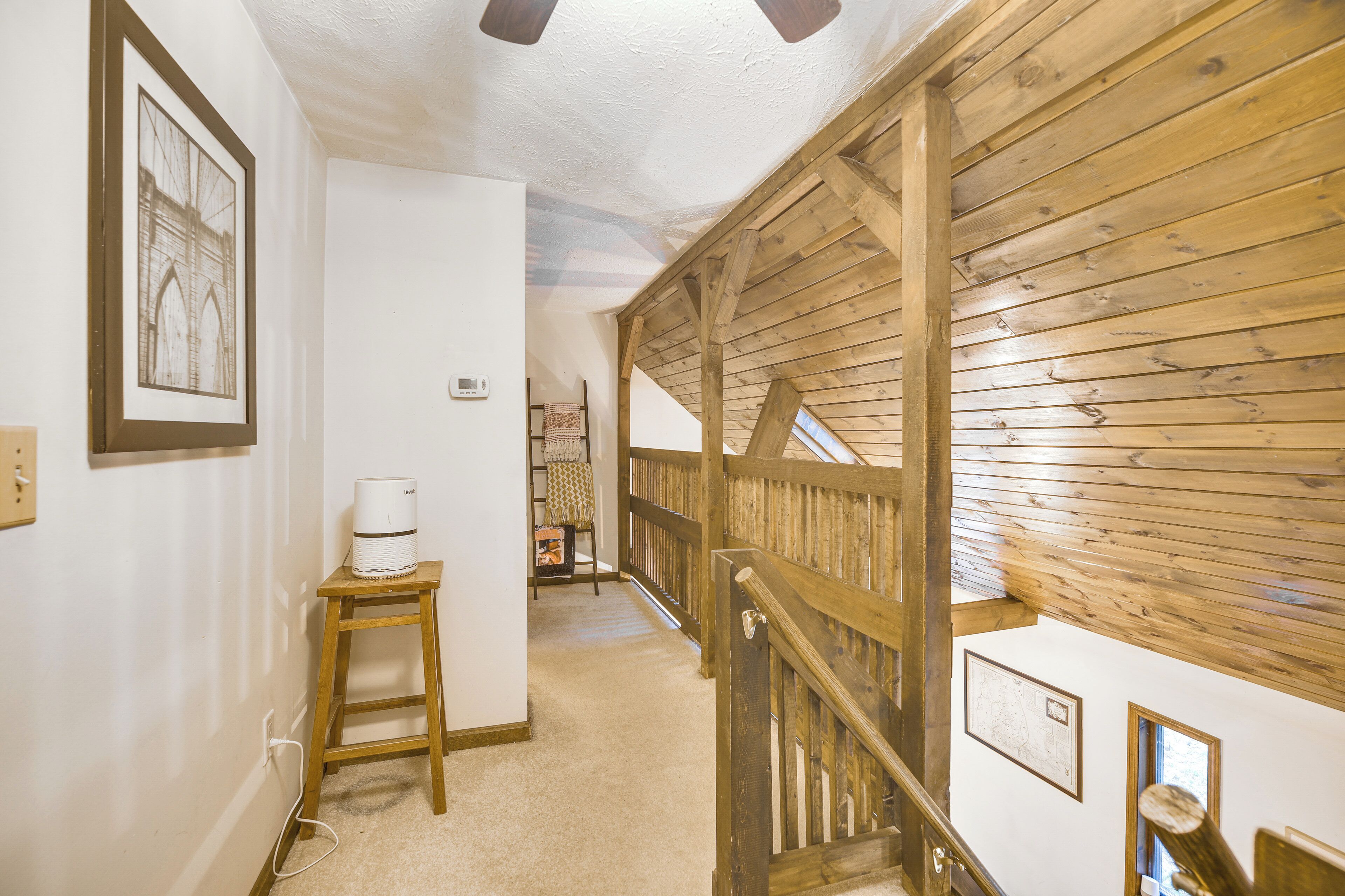 A hallway with a wooden staircase, a white wall with a framed picture, and a small table with a white device.