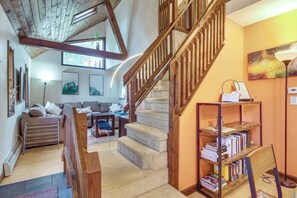 Un vaste espace de vie comprenant un escalier en bois, un ensemble de canapés et une bibliothèque.
