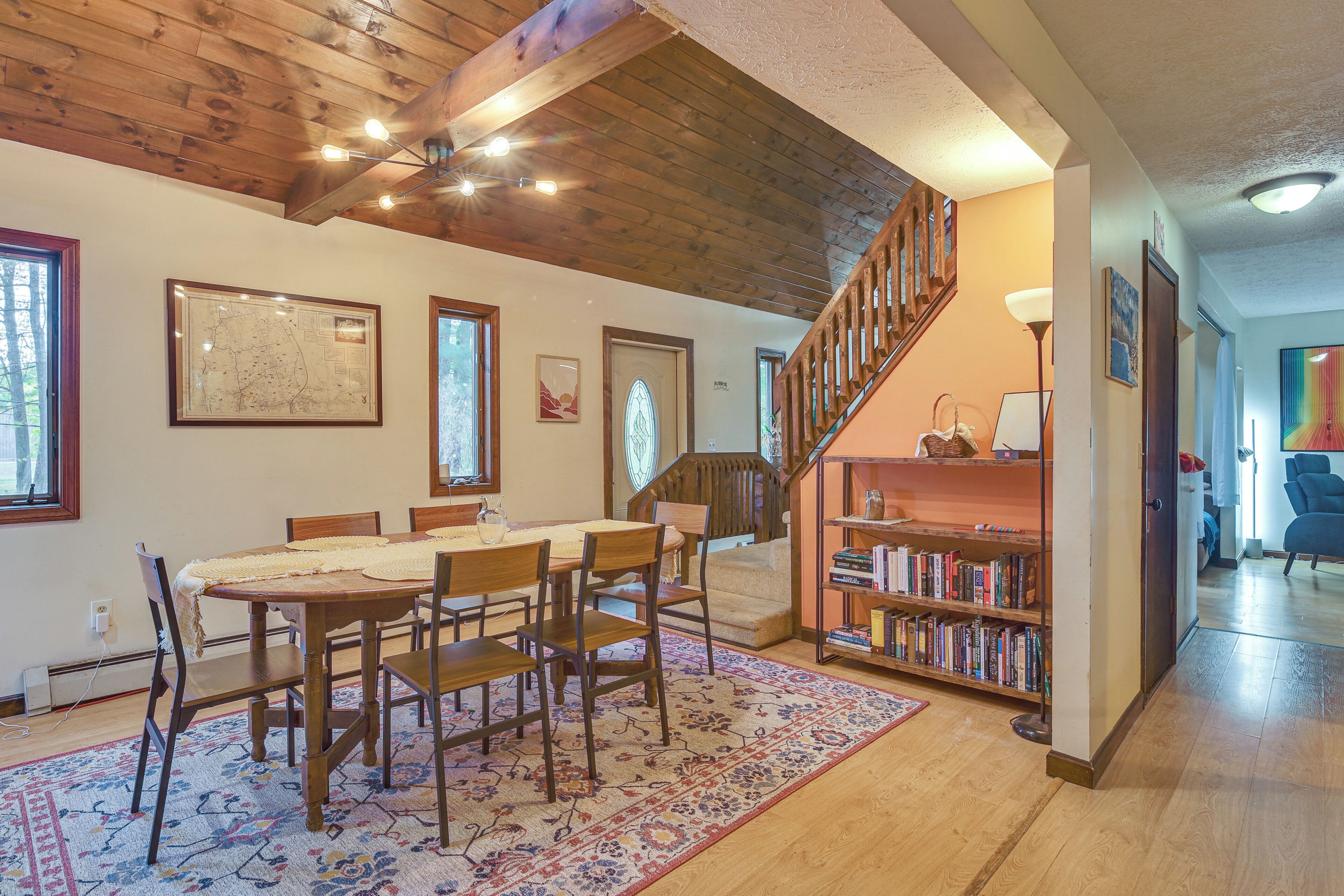 Un comedor con mesa y sillas de madera, una estantería y una escalera que sube a otro nivel.