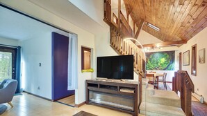 Una sala de estar con televisión de pantalla plana, escalera de madera y comedor con vistas a un bosque.