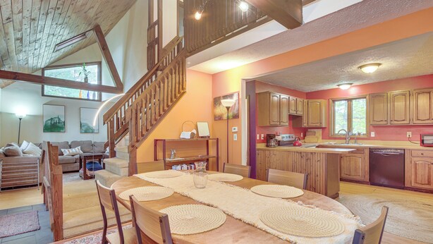 Un comedor amplio con una larga mesa de madera, rodeado de sillas, y una escalera que lleva a un nivel superior.