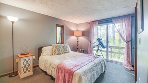 Un dormitorio con cama, mesita de noche, lámpara, ventana con cortinas y vista al exterior.