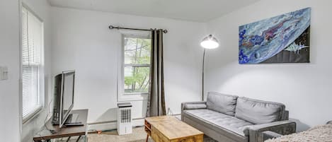 Una sala de estar moderna con un sofá gris, una mesa de centro de madera, un televisor sobre un mueble bajo y un cuadro en la pared.