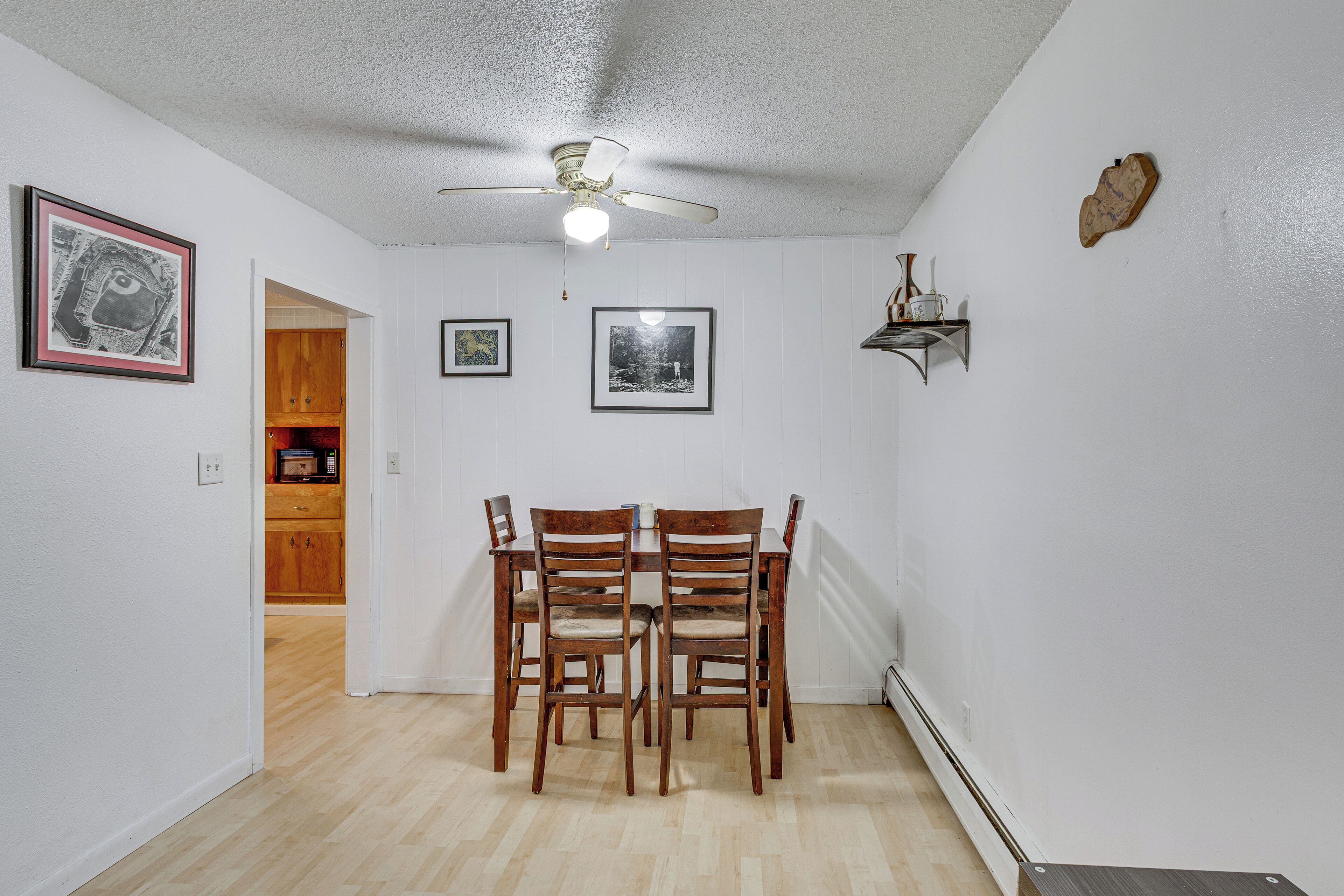Un comedor con una mesa y sillas, un ventilador de techo y cuadros en la pared.