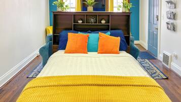 A bed with orange and blue pillows, a yellow throw blanket, and a wooden headboard with shelves.