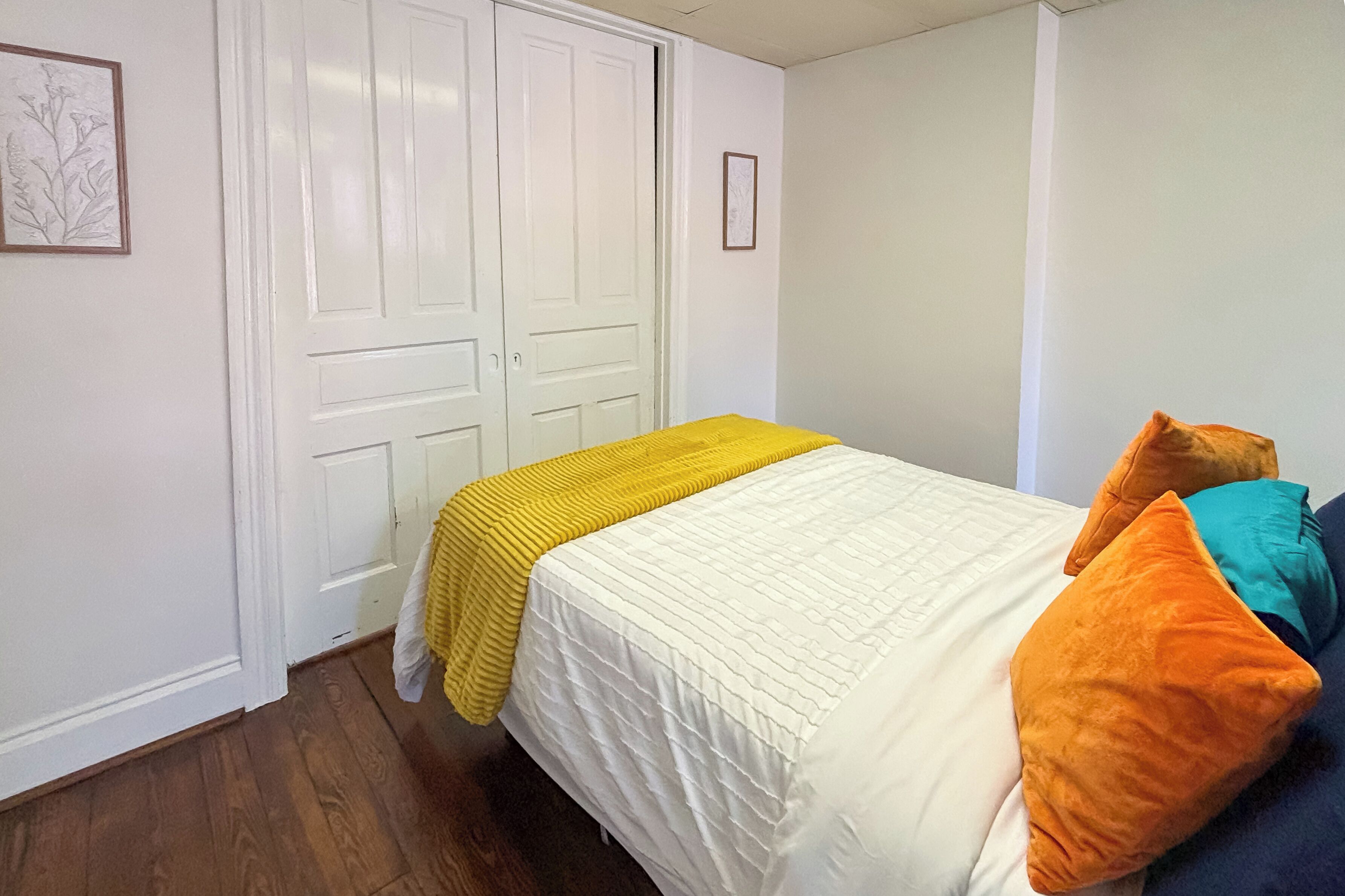Ein Schlafzimmer mit einem Bett, einer gelben Decke und orangefarbenen Kissen.
