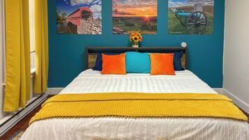 A bedroom with a bed, yellow and blue pillows, a yellow throw blanket, and three wall art pieces depicting animals and a sunset.