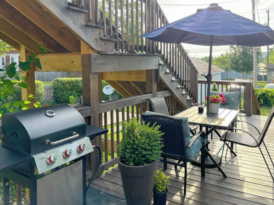 Una terraza de madera con una parrilla, mobiliario exterior y una planta en maceta.