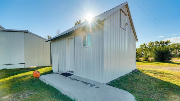 A single-story metal building with a small window and a door, a concrete pathway leading to the entrance, and a pumpkin decoration on the grass. - Pet-friendly Farmhouse Suite w/ Patio in Vaughn! (Vaughn)