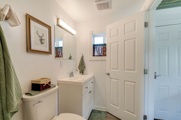 A bathroom with a toilet, sink, mirror, and a framed deer head picture.