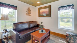 A living room with a brown leather sofa, a wooden coffee table with a vase, and a framed picture on the wall. - Pet-friendly Farmhouse Suite w/ Patio in Vaughn! (Vaughn)