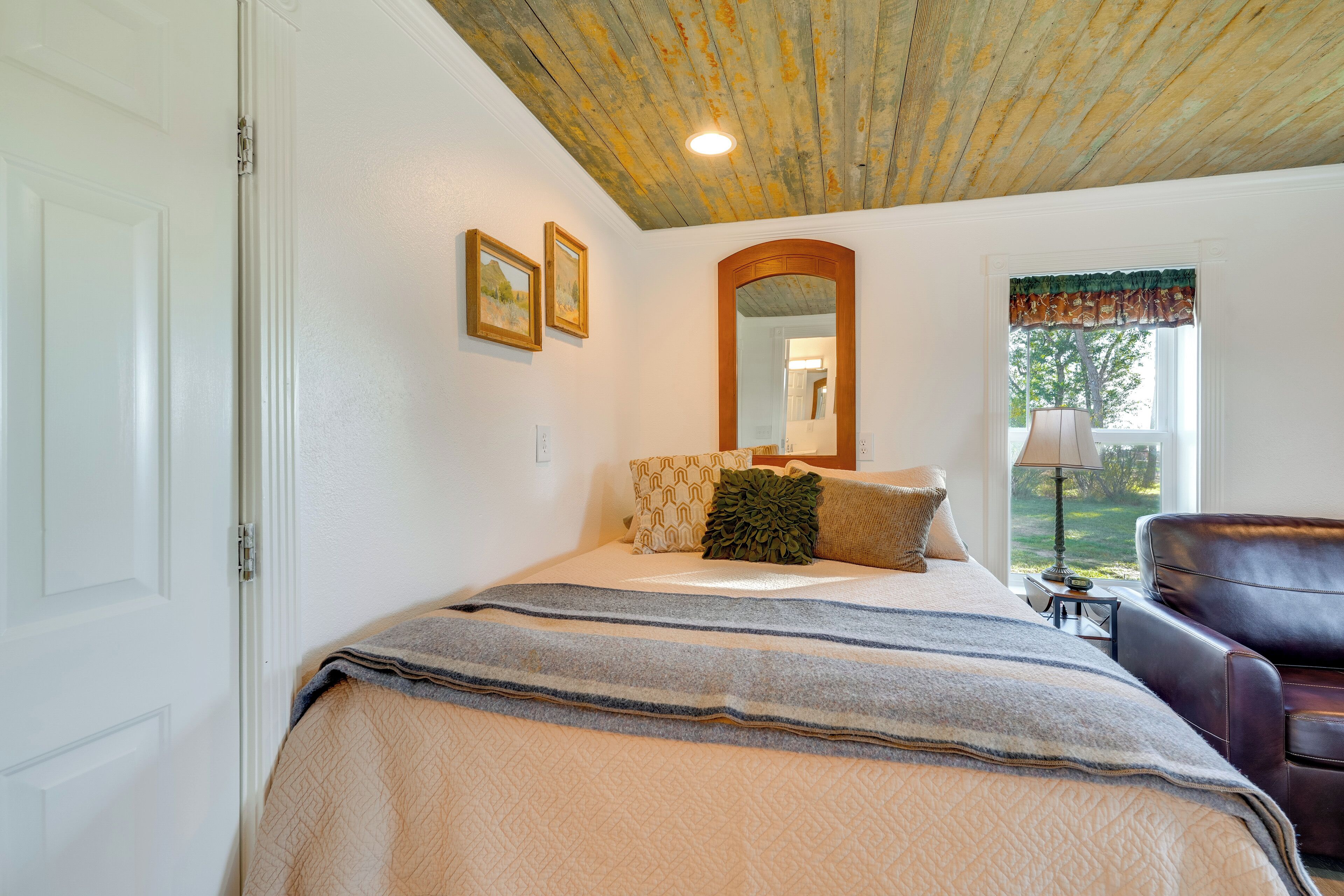 Une chambre à coucher avec un lit, une chaise, une fenêtre donnant sur un beau paysage et un plafond avec des poutres apparentes.