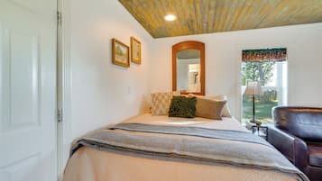 Un dormitorio con cama, una silla, ventana con vistas y techo con vigas a la vista.