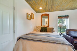 Un dormitorio con cama, una silla, ventana con vistas y techo con vigas a la vista.