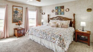 Une chambre à coucher avec un grand lit, un ventilateur de plafond, une table de chevet avec une lampe, une commode et une fenêtre avec des rideaux.