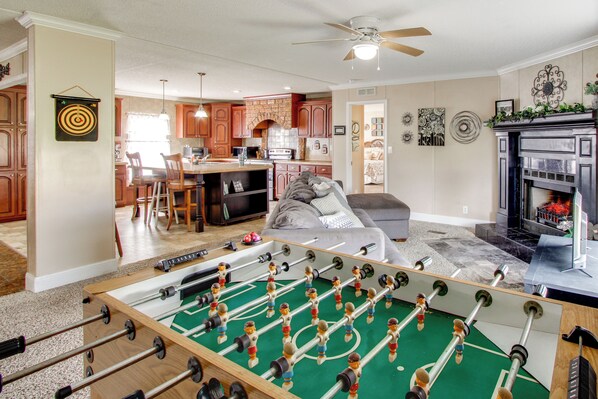 Una sala de estar con mesa de fútbol, chimenea y una cocina al fondo.