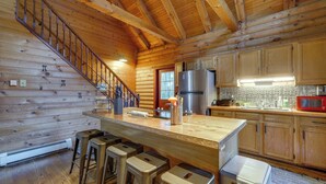 Eine Kücheneinrichtung in einer Blockhütte mit Holzwänden, einer Holztreppe, einem Edelstahlkühlschrank und einer Bar mit Hockern.