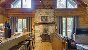 Ein Blockhaus-Interieur mit Kamin aus Naturstein, Holzmöbeln und großen Fenstern.