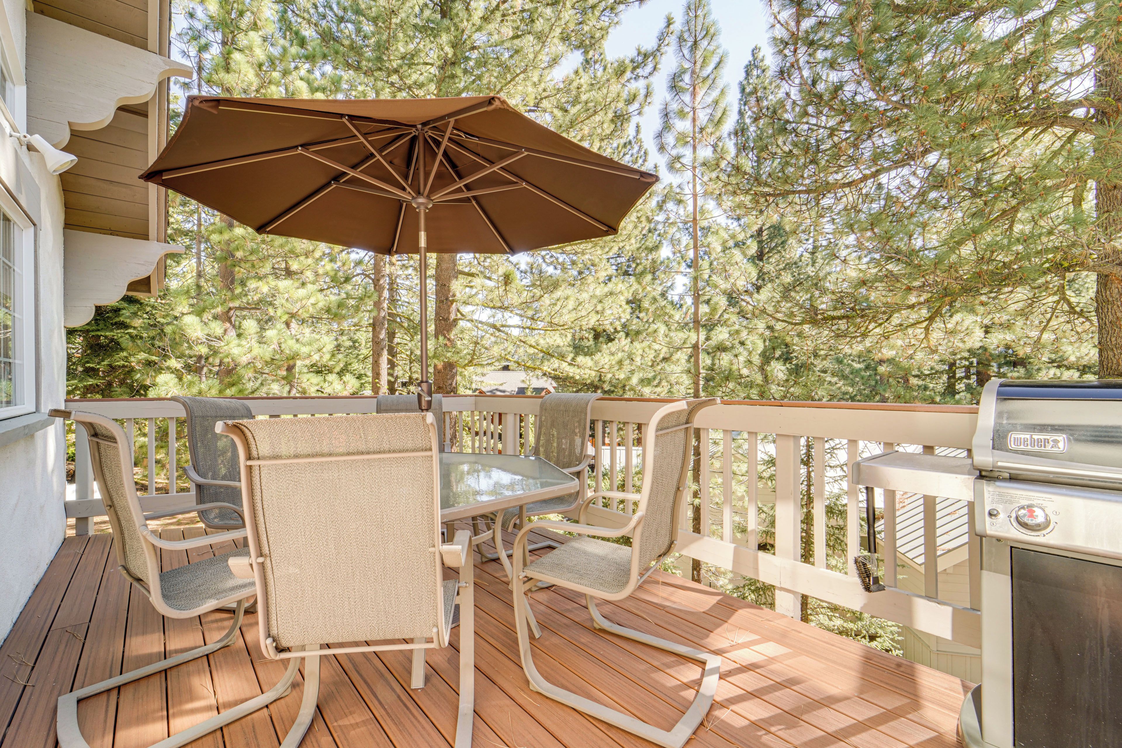 A deck with a table and chairs, an umbrella, and a grill.