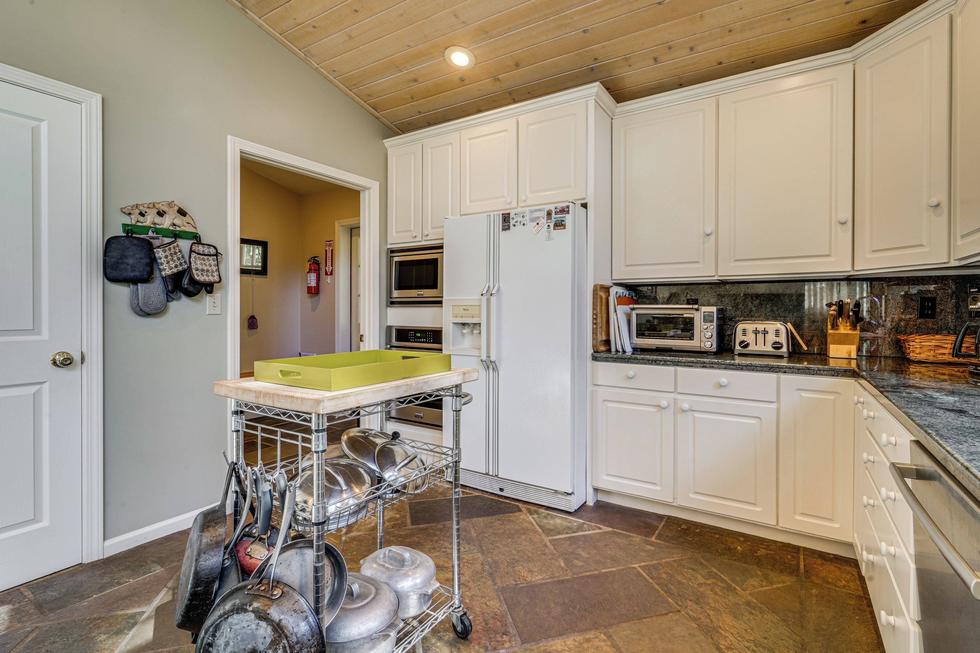 A kitchen with white cabinets, a microwave, a refrigerator, a toaster, and a cart with pots and pans.