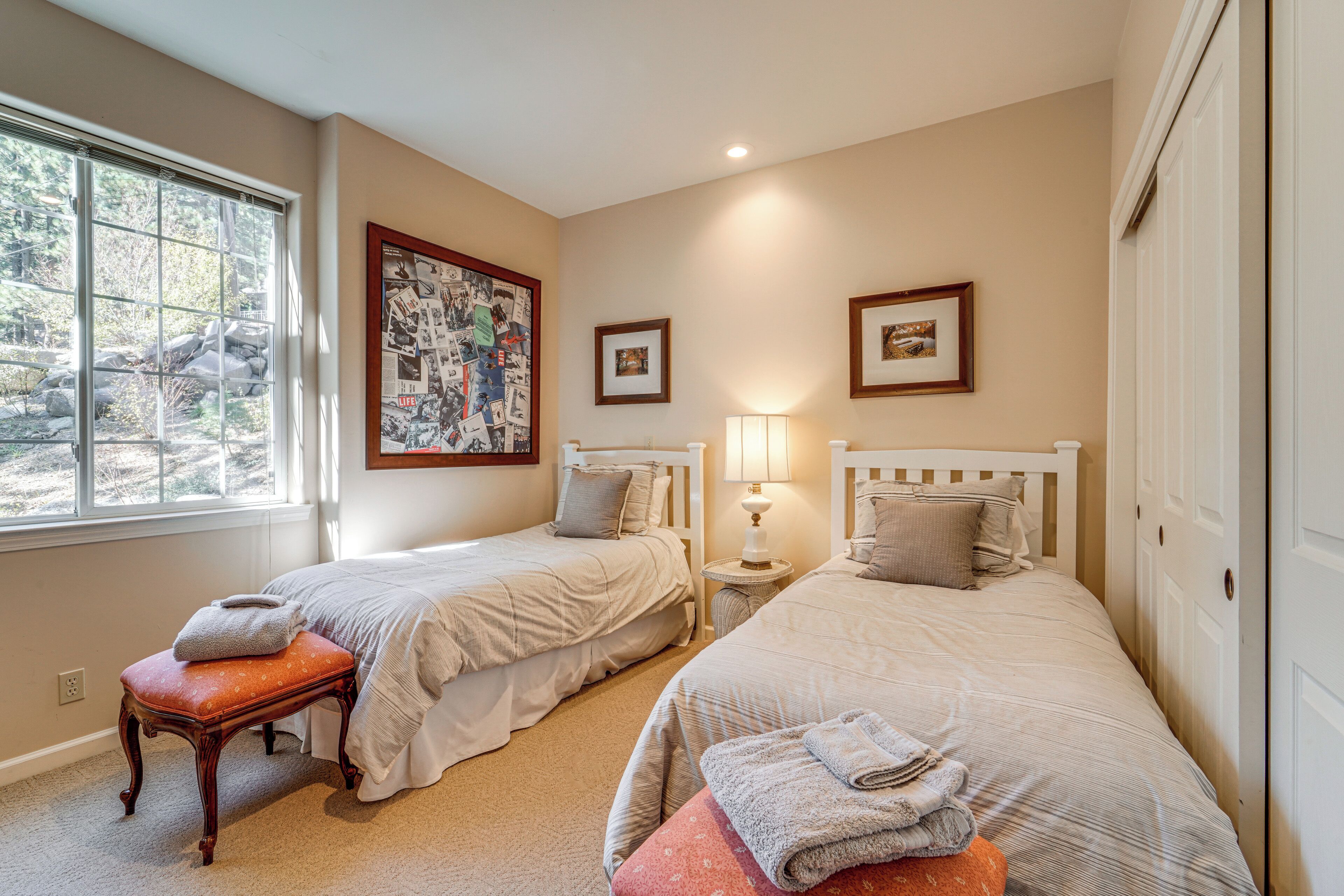 A bedroom with two beds, a window with a view of rocks, and a framed collage on the wall.