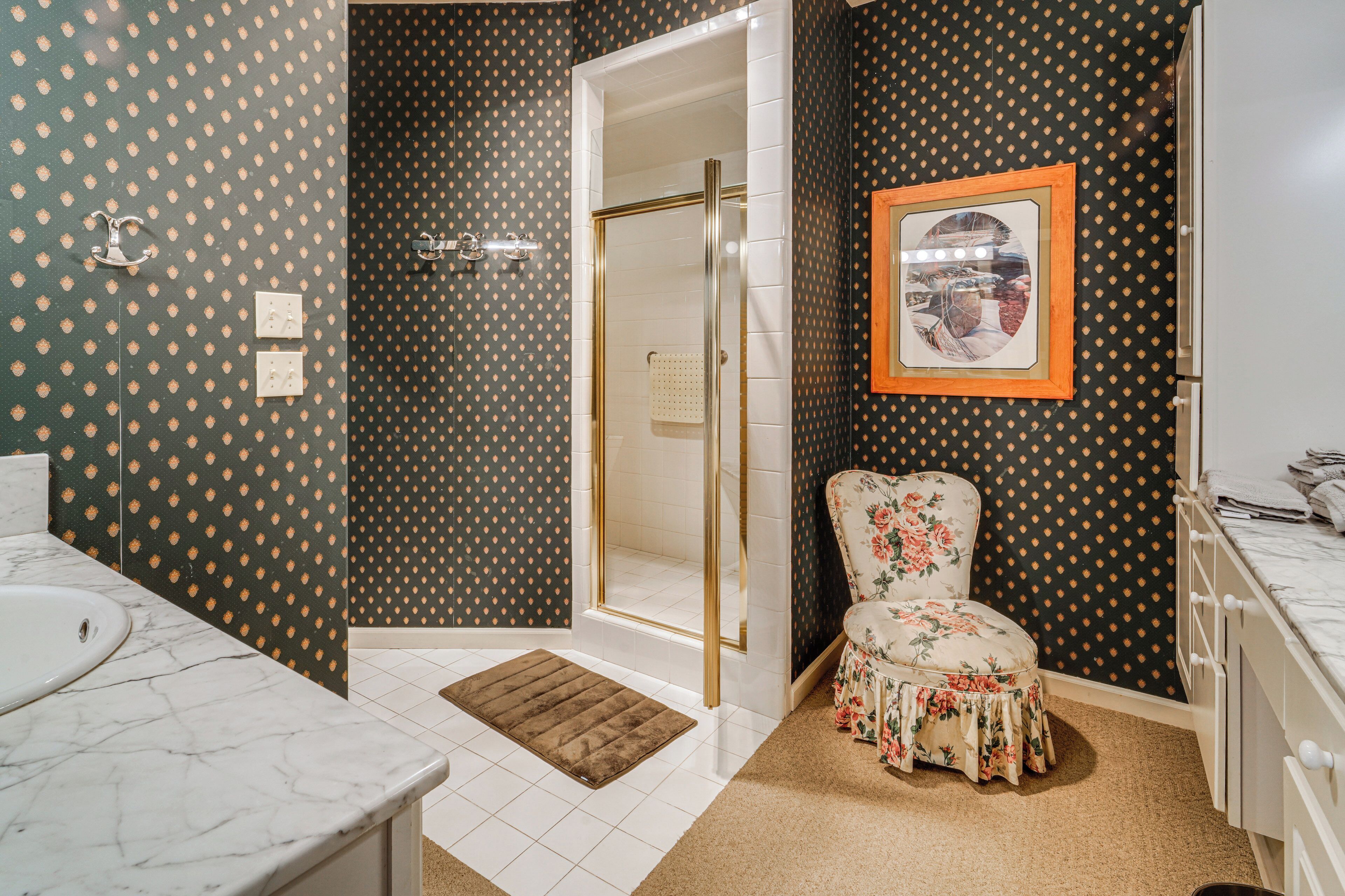 A bathroom with a shower, a sink, a toilet, and a chair.