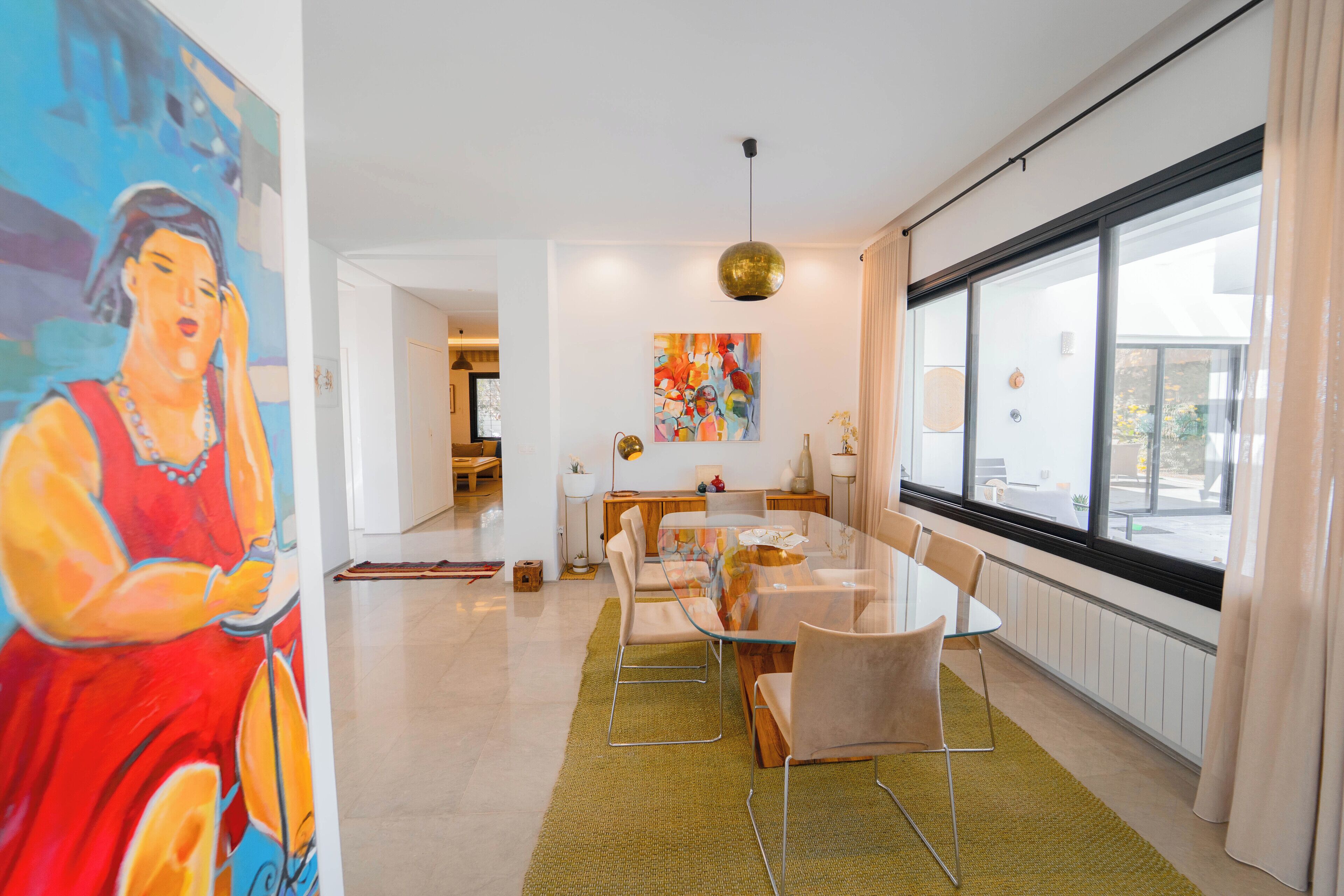 Uma área de jantar moderna com mesa de vidro, cadeiras e obras de arte nas paredes.