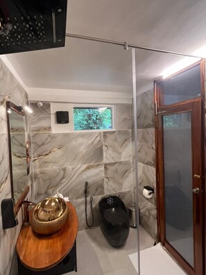 Une salle de bain avec un mur en marbre, un meuble-lavabo en bois, des toilettes noires et une cabine de douche en verre.