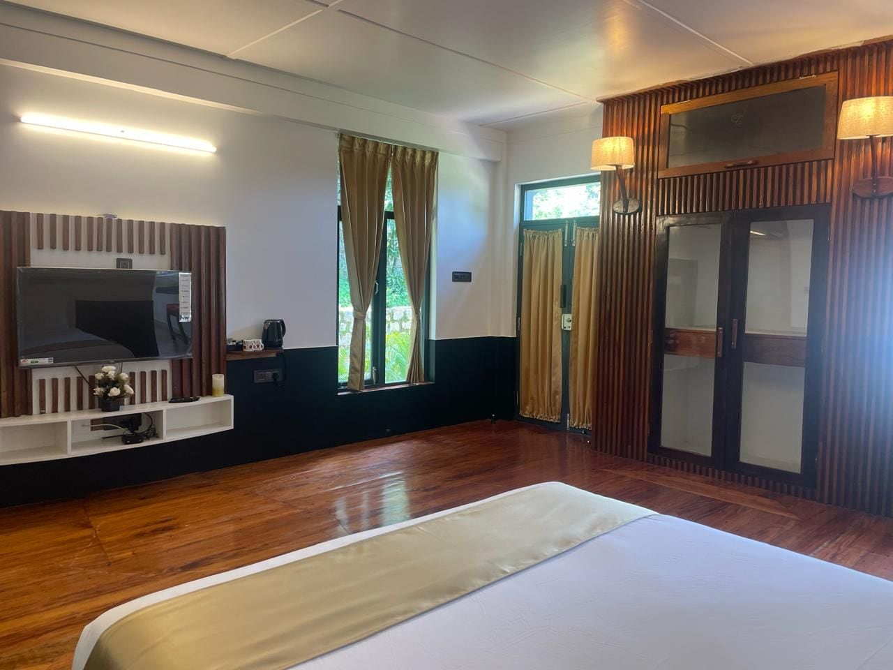 A hotel room with a bed, a TV, a window with curtains, and a sliding door.