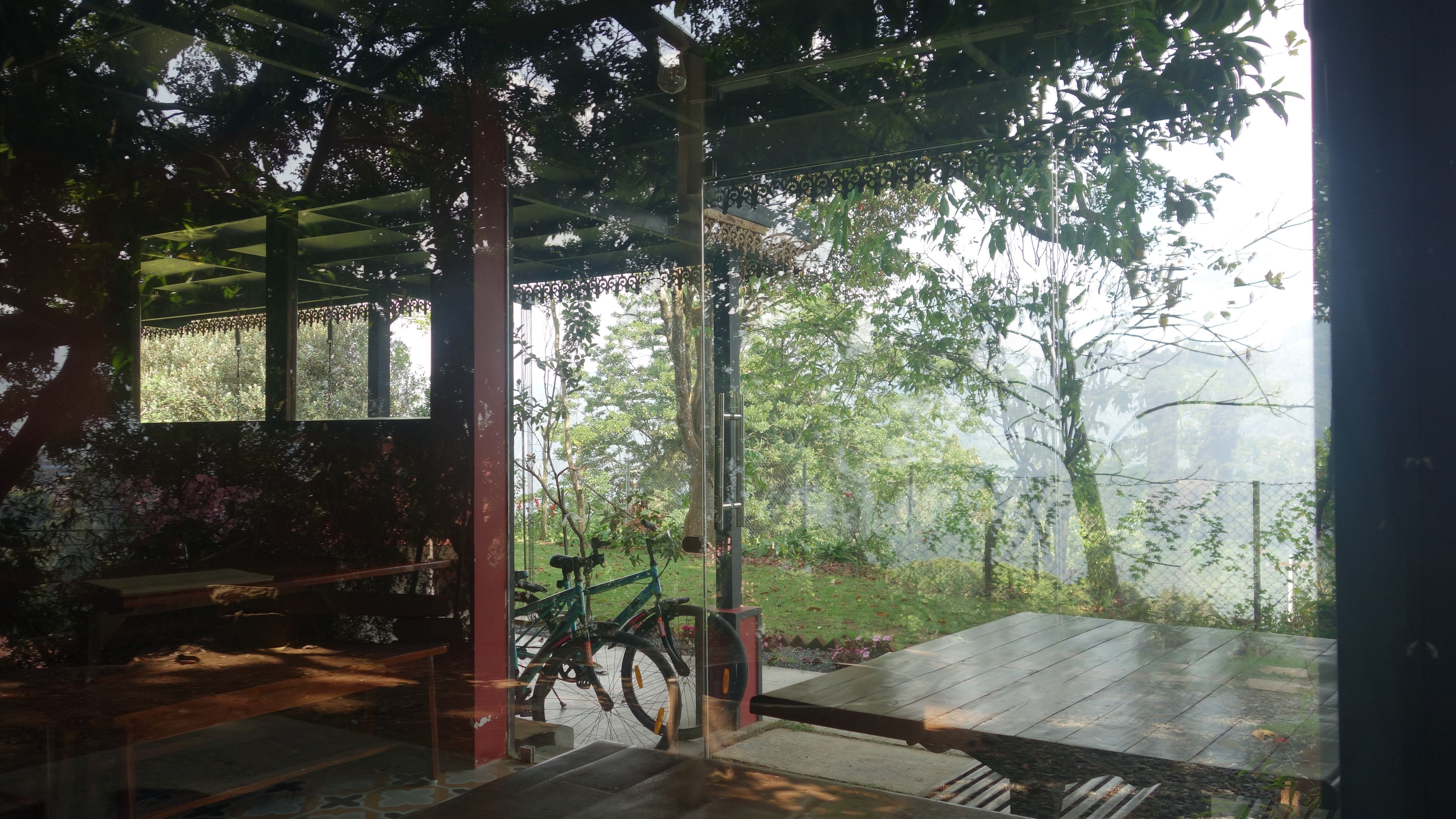 Un espace extérieur abrité avec des sièges, un vélo, des bancs en bois et une vue sur un jardin.
