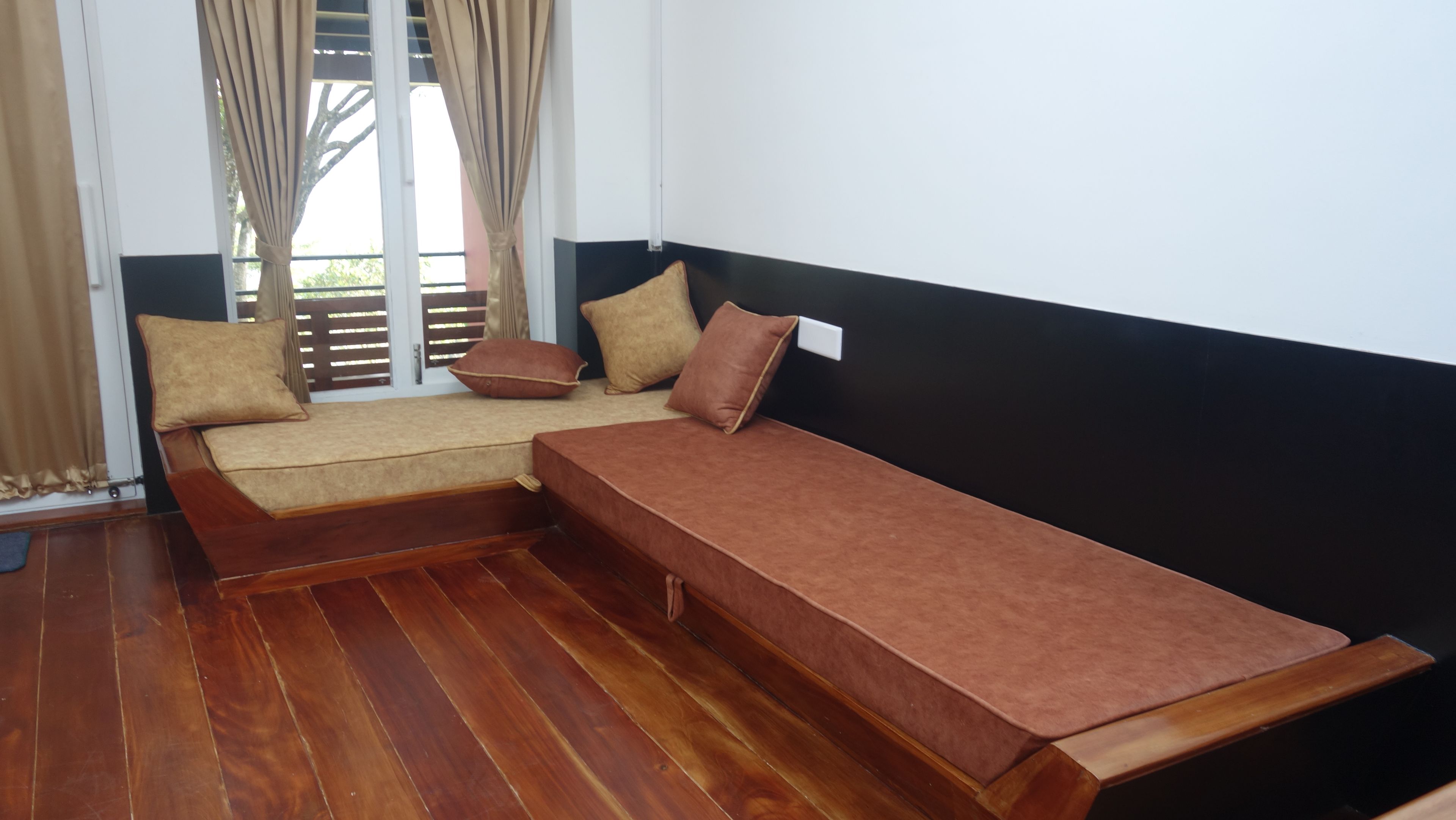 A room with a sofa bed, a wooden floor, and a window with curtains.