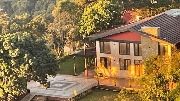 Una casa moderna con techo rojo, rodeada de exuberante vegetación y colinas.