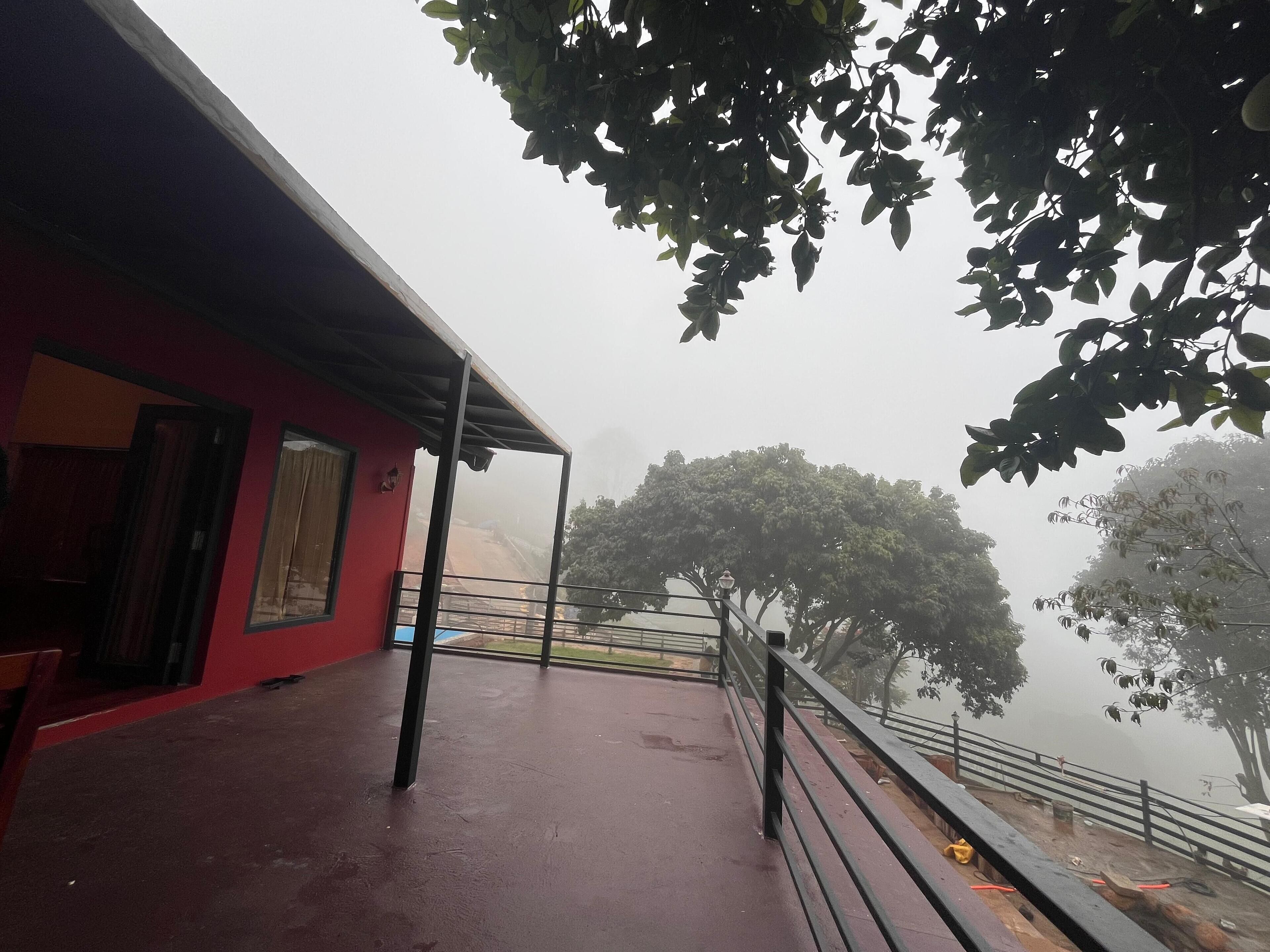 A red building with a covered balcony, a metal railing, and a view of trees through fog.