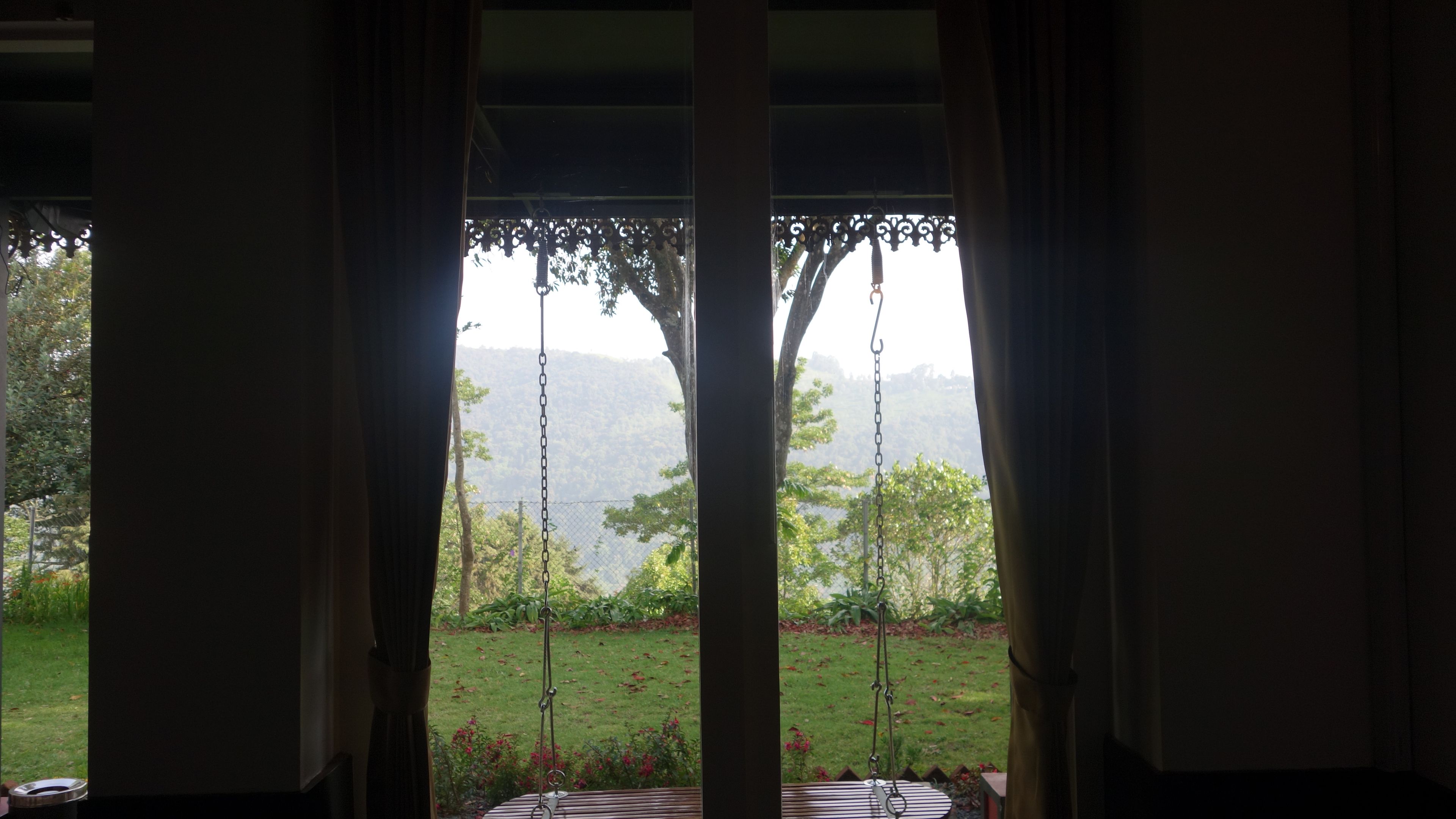 A room with a view of a garden and mountains through curtains.