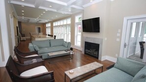 A spacious living room with a fireplace, a television mounted on the wall, and a large window providing natural light. - Luxury Construction With A Private Pool (Rehoboth Beach)
