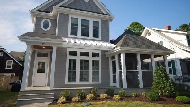 A two-story house with a covered front porch, a garage, and a small front yard with landscaping. - Luxury Construction With A Private Pool (Rehoboth Beach)