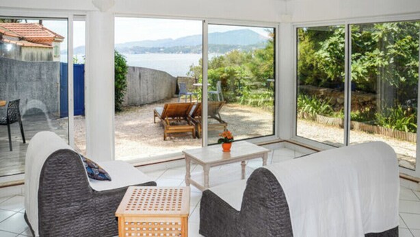 A modern room with a large sliding glass door leading to a patio with outdoor furniture. - Apartment with a view of the garden and an unobstructed view of the ocean! (Le Pradet)
