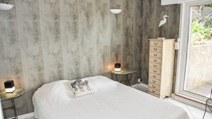 A bedroom with a bed, a dresser, a nightstand, and a wall-mounted lamp. - Apartment with a view of the garden and an unobstructed view of the ocean! (Le Pradet)